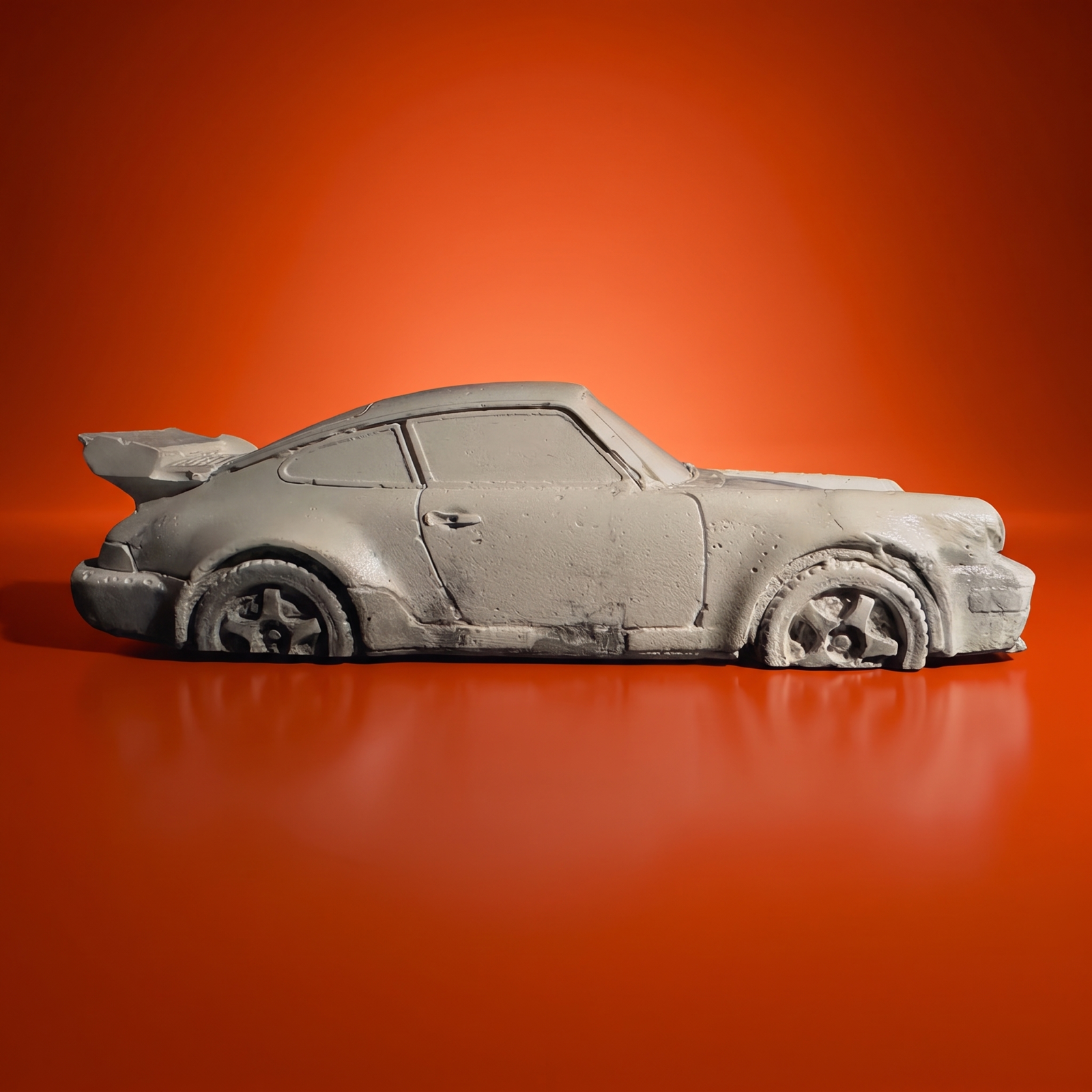 The rear-engined concrete coupe in side profile on an orange studio backdrop