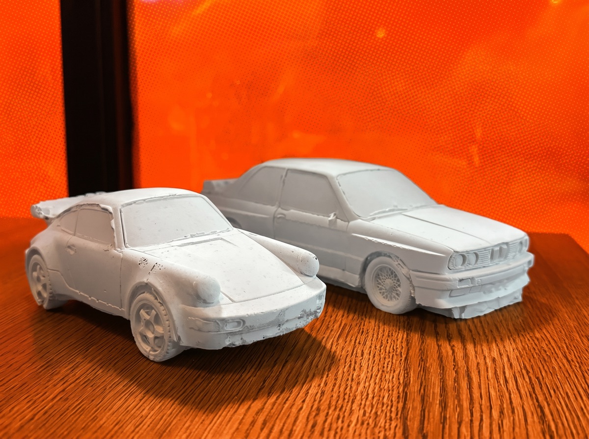 The concrete saloon and coupe together on a hazard-orange field